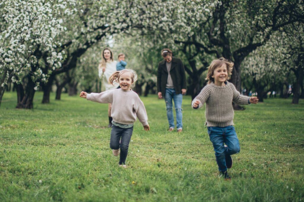 Eine Familie mit drei Kindern im Sommer auf einer Wiese. Zwei der Kinder rennen richtung Kamera